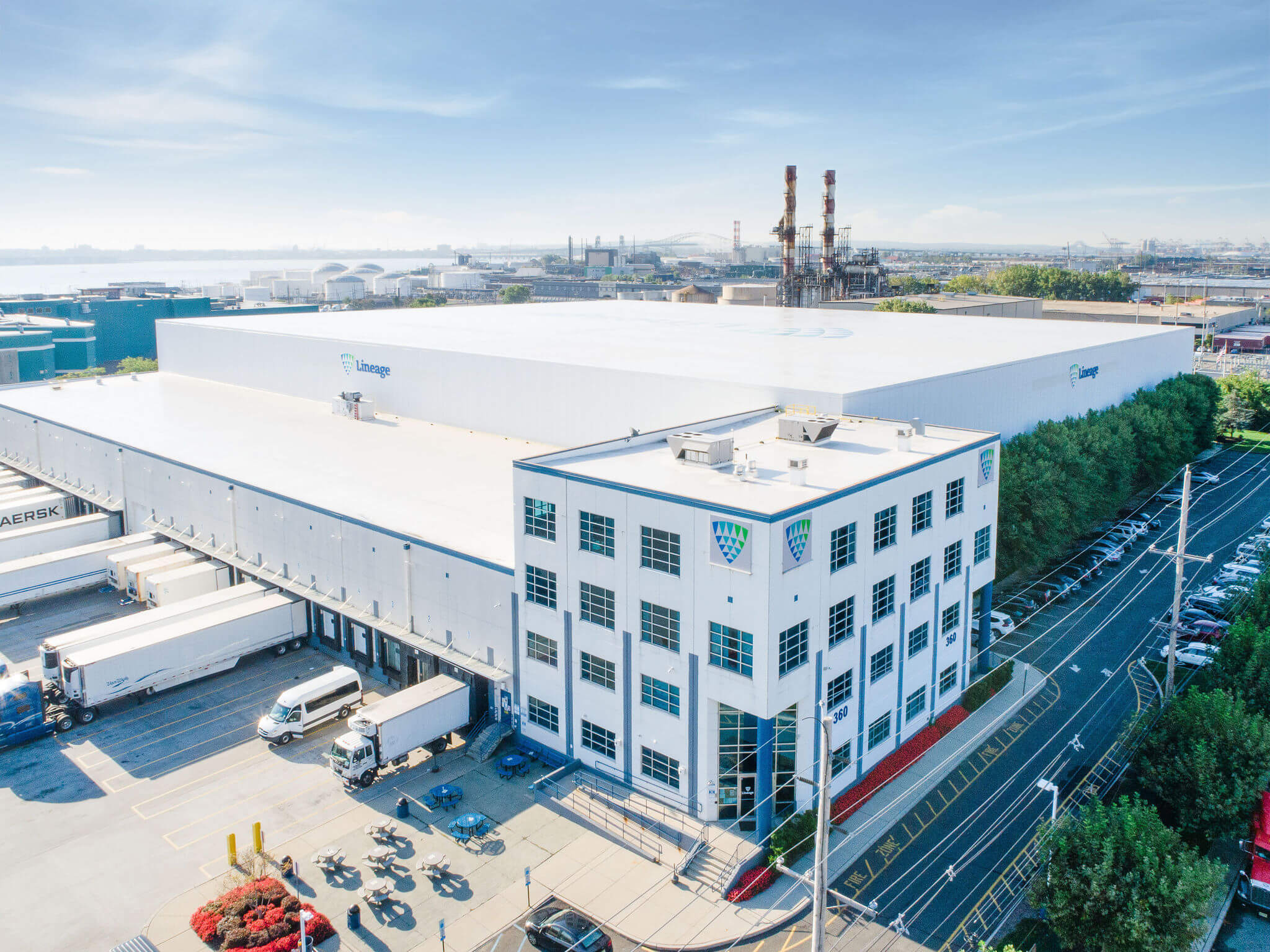 An aerial view of a large Lineage cold storage warehouse facility with parked trailers and a clear blue sky.