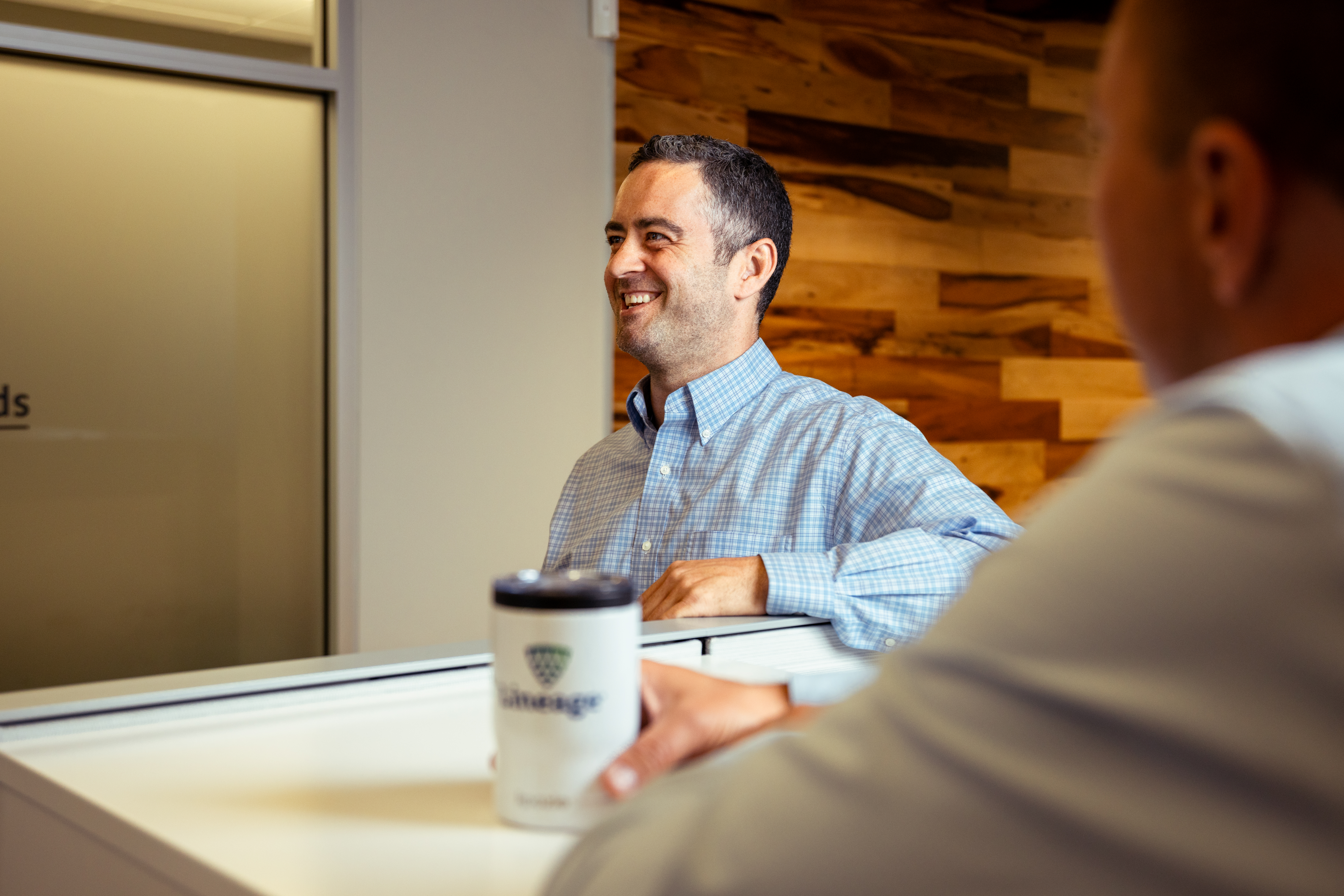 Man smiling in chequered button down shirt at a Lineage office