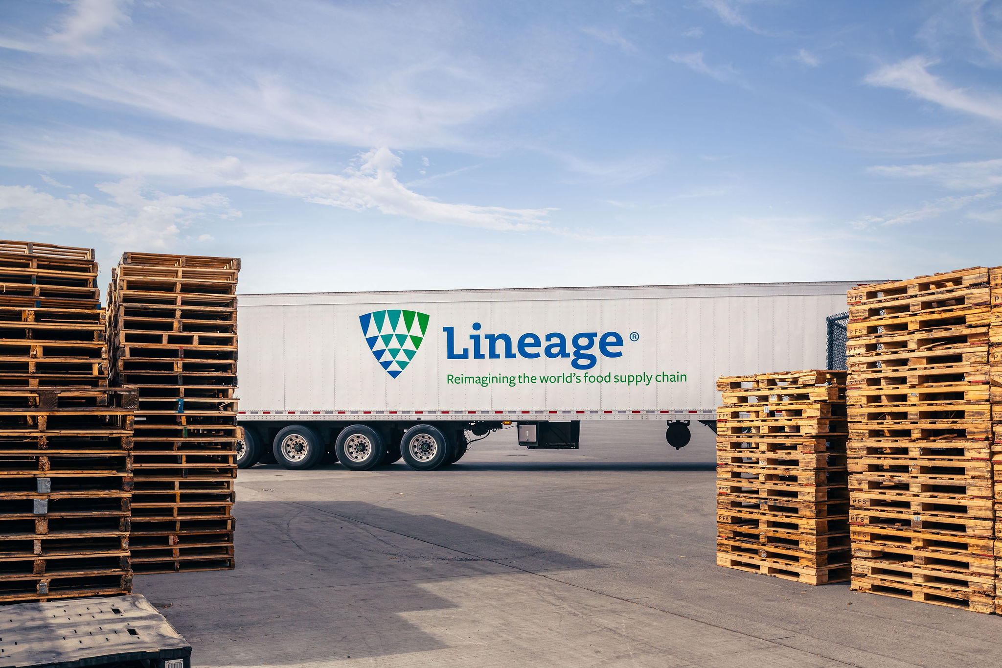 Lineage truck seen behind stacks of wooden pallets