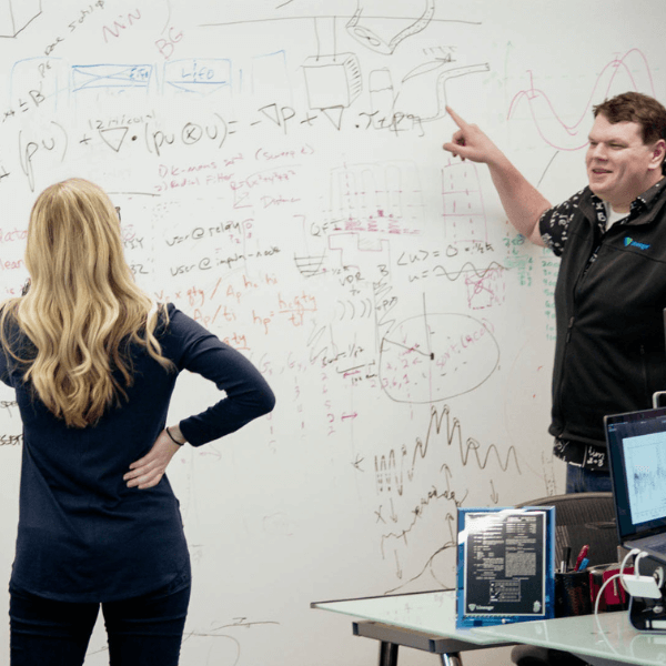 Data scientists discussing complex algorithms and solutions on a whiteboard in a collaborative office environment.