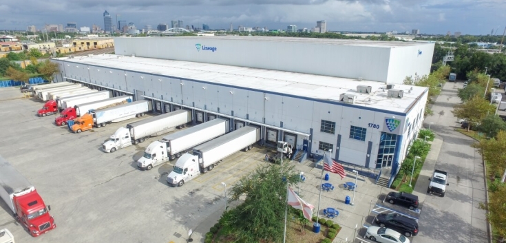 Exterior shot of Lineage's West Beaver cold storage warehouse in Jacksonville with multiple trucks at the loading bays, under a cloudy sky. 