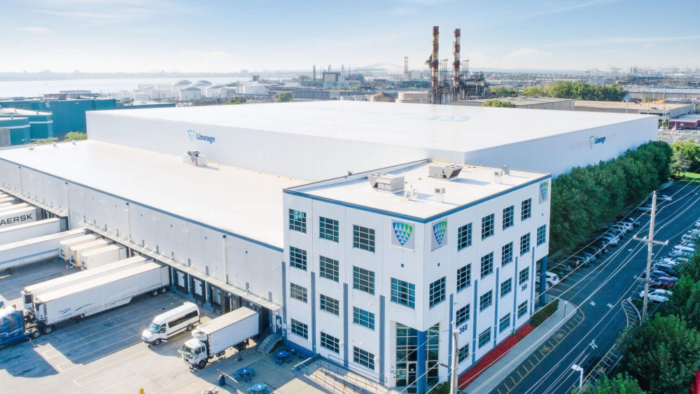 An aerial view of a large Lineage cold storage warehouse facility with parked trailers and a clear blue sky.