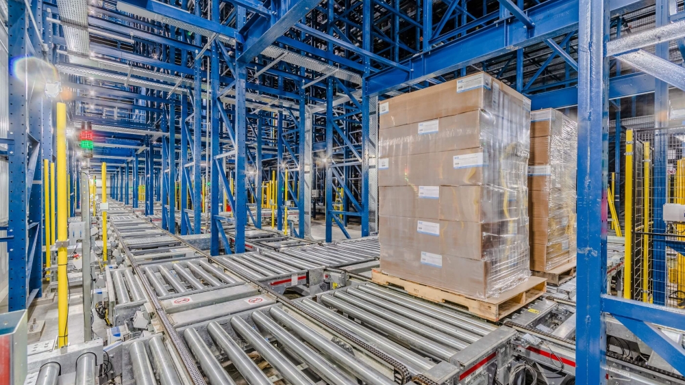 Lineage Sunnyvale automated warehouse interior with conveyor belts transporting shrink-wrapped pallets, flanked by tall blue steel racks.