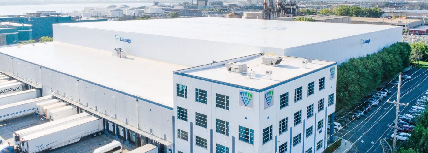 An aerial view of a large Lineage cold storage warehouse facility with parked trailers and a clear blue sky.